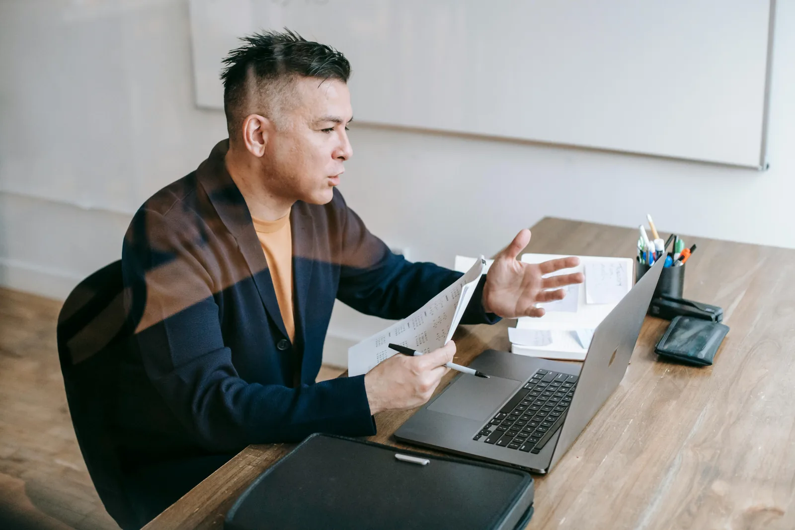 Leader in conversation across a desk, laptop open, gesturing mid-discussion